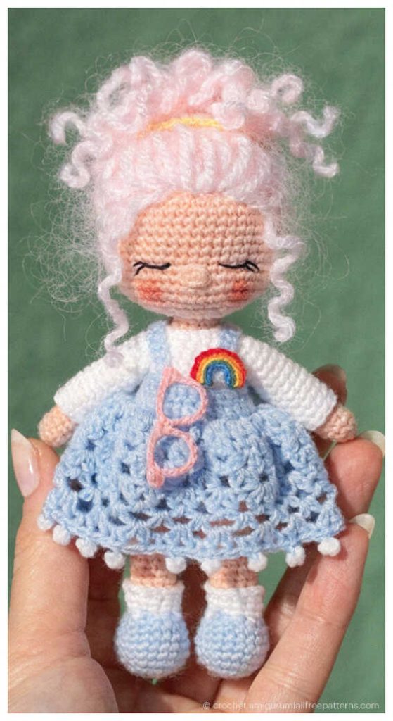 Crochet doll with pink curly hair and a blue lace dress held in hand, styled as a cute handmade gift for girls