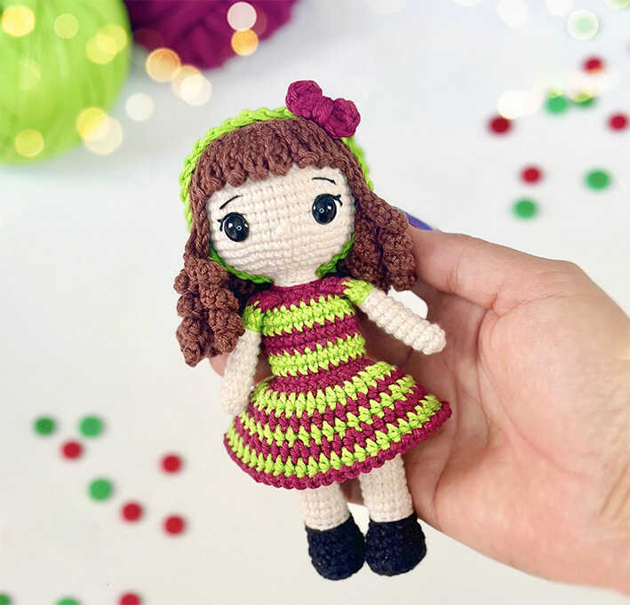 Arbella crochet doll held in hand with curly hair and striped dress, designed as a handmade kids gift and shown as a free crochet pattern