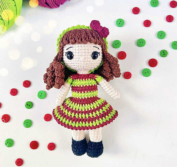 Cute Arbella crochet doll with curly hair and striped dress, designed as a handmade gift idea and shown as a free crochet pattern